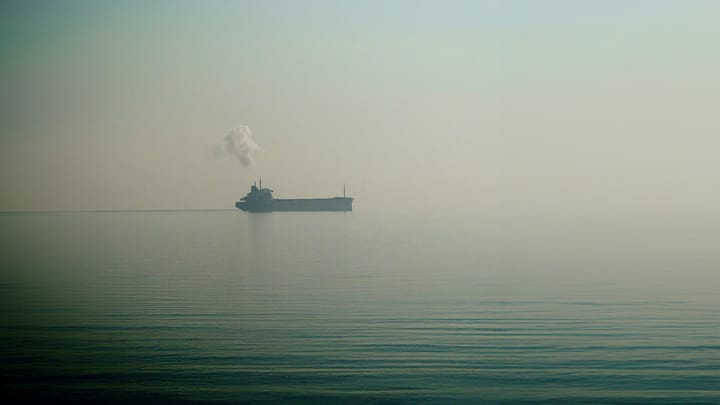 A cargo ship in the distance during the faint break of a foggy day